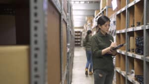 Inventory specialist taking stock in a warehouse with organized shelving units filled with inventory boxes.