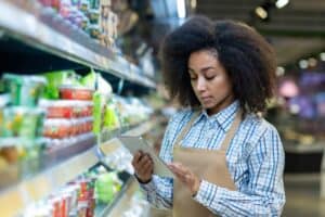 Fresh produce inventory management at a grocery store with a store employee using a tablet for stock control.